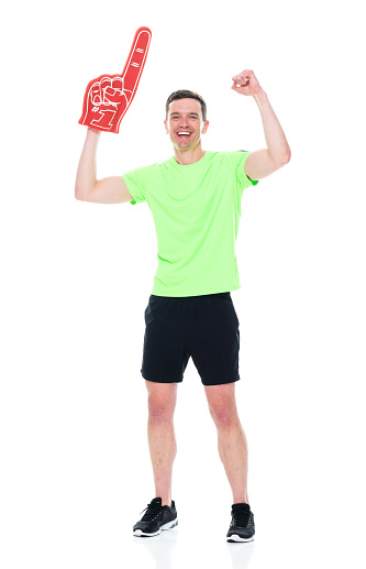 Full length of aged 30-39 years old who is tall person with short hair caucasian male fan - enthusiast exercising in front of white background wearing shirt who is showing cool attitude and cheering who is pointing and holding foam hand