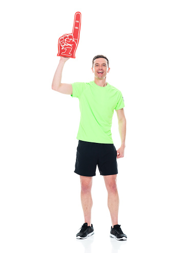 One person of aged 30-39 years old who is slim with short hair caucasian male fan - enthusiast standing in front of white background wearing t-shirt who is showing cool attitude and cheering who is pointing and holding foam hand