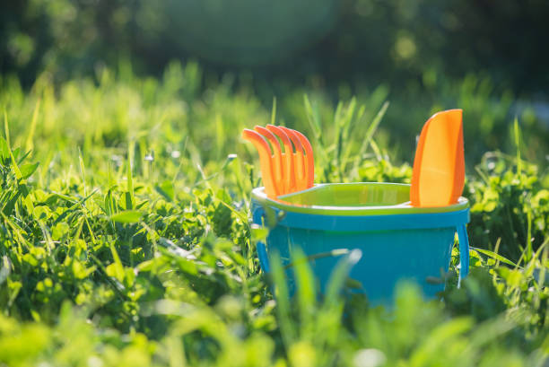 Baby toys a bucket with rake and shovel on the green grass background.