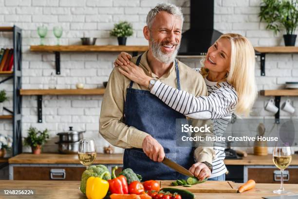 Senior Couple Spending Time Together While Cutting Vegetables At Kitchen Stock Photo - Download Image Now