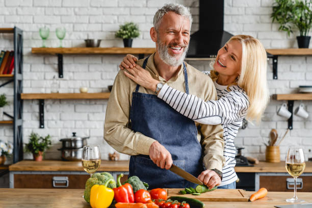 senior couple spending time together while cutting vegetables at kitchen - cooking senior adult healthy lifestyle couple imagens e fotografias de stock