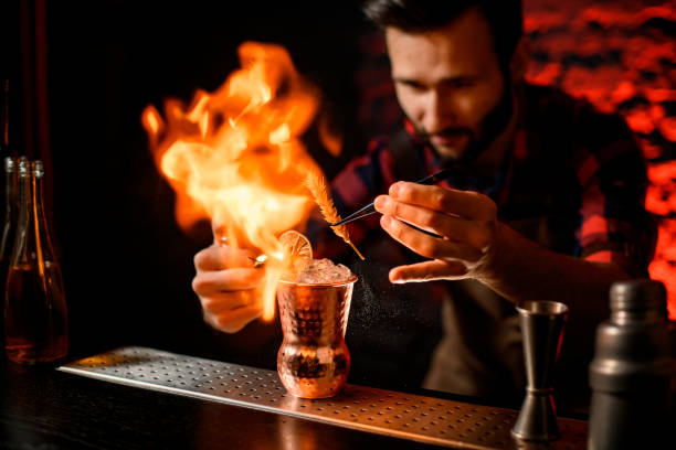istock bartender holds tweezers with spikelet over metal cup and makes fire flame. 1248256468