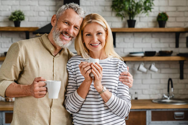 Beautiful middle aged couple drinking tea or coffee at home while looking at camera