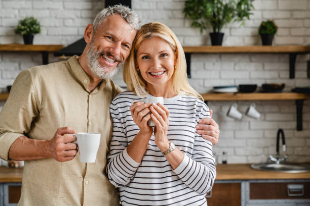 beautiful middle aged couple drinking tea or coffee at home while looking at camera - coffee cafe drinking couple imagens e fotografias de stock