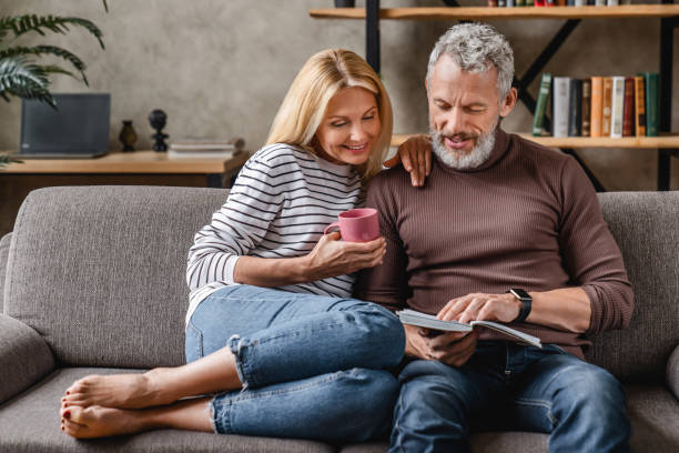 自宅で休んでいる間にソファで本を読む成熟したカップル - sofa couple relaxation comfortable ストックフォトと画像