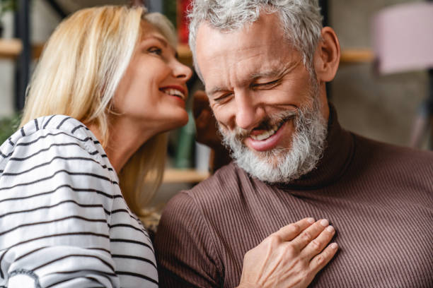 senior mann lächelnd, während seine schöne liebevolle frau flüstert zu seinem ohr - attractive couple stock-fotos und bilder