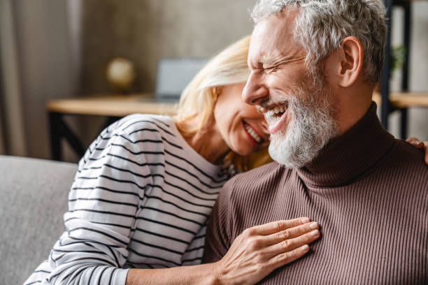 felice ridere coppia di mezza età legare mentre si rilassa seduto sul divano - couple loving married affectionate foto e immagini stock