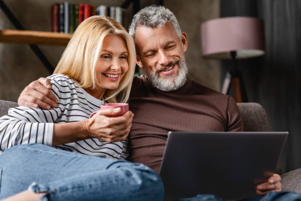 istock Happy beautiful middle aged couple using laptop and smiling while resting on couch at home 1248256773