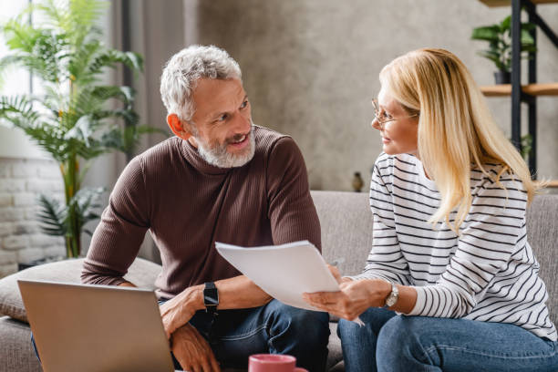 istock Smiling middle aged couple with laptop studying documents while working on couch at home 1248256822