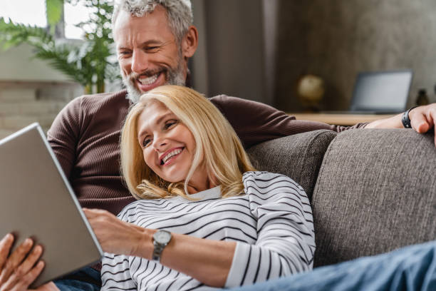 istock Close up of smiling middle aged couple using digital tablet on couch at home interior 1248256845