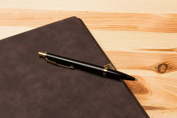 Top view mockup template with a Parker pen and  notebook laying on wooden background.