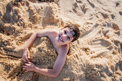 Boy burying himself on the beach sand