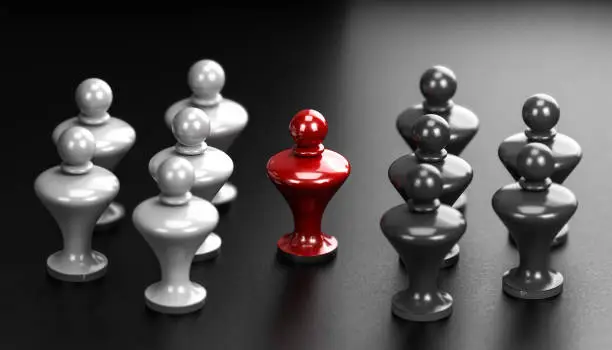 Photo of Concept of pawns representing conflict between groups and one mediator in the middle.