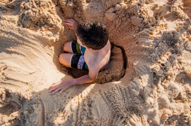 istock Boy burying himself on the beach sand 1248259368