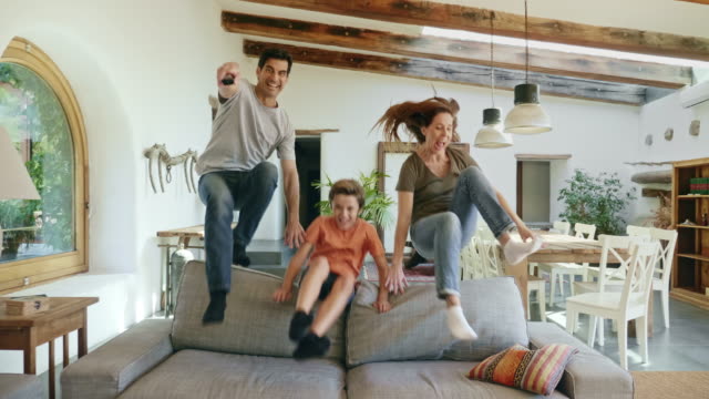 Parents with son jumping over back of sofa to watch tv