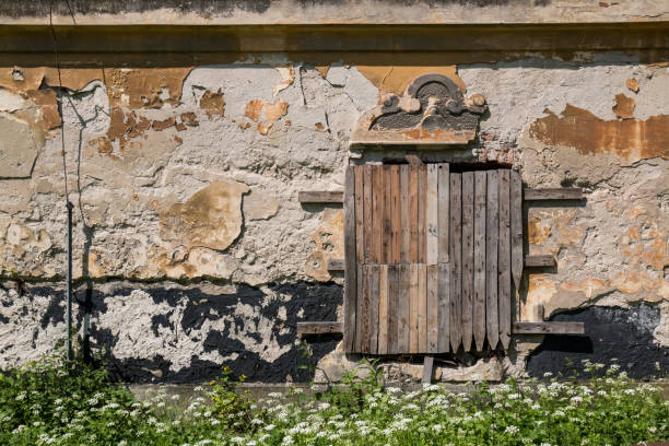 Weathered and peeled off facade of an abandoned manor house. Window covered by wooden laths. Jablonica, Slovakia.