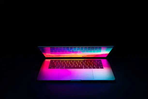 Photo of Isolated high tech open laptop with abstract vibrant color screen on a dark background.