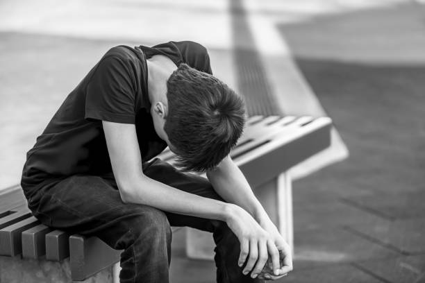 sad teenager male sitting on a bench sad teenager male sitting on a bench. black and white sad teenager boy crying outdoors in park stock pictures, royalty-free photos & images