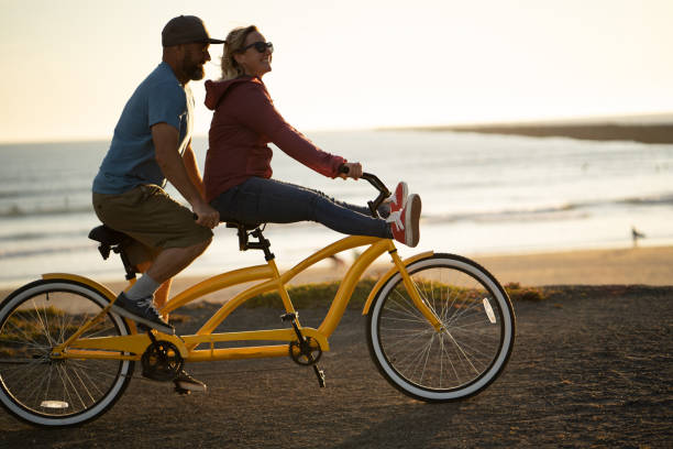 jeune couples ride vélo tandem au lever du soleil - candid people casual bicycle photos et images de collection