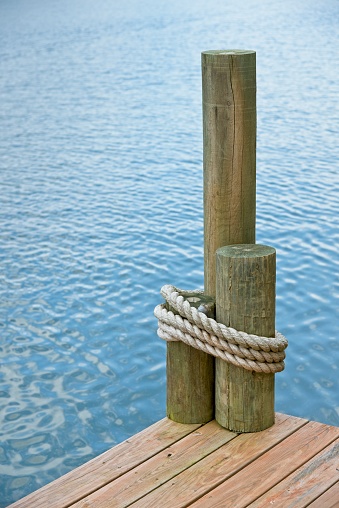The corner of a boat dock, on a lake, with rope wrapped around pilings.