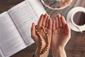 top view female hand of prayer with wooden beads in sunlight, iftar concept, Ramadan month, Koran, plate of dried fruit, Cup of tea on wooden table