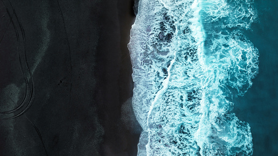 Aerial view of turquoise colored wave splashing to black sand beach