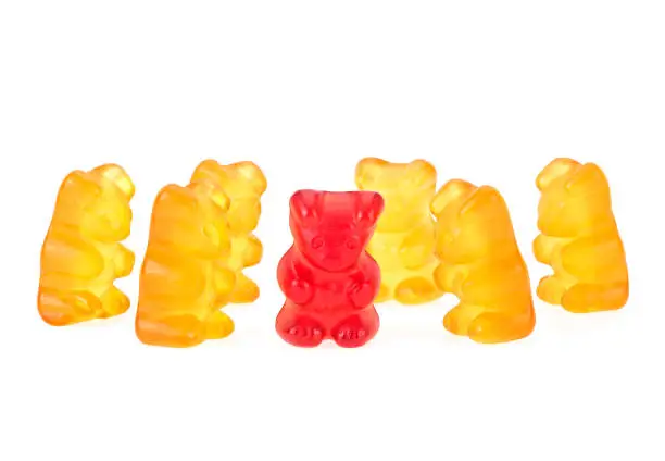 Photo of Yellow gummy bears and a single red one on a white background. Children's multivitamin.