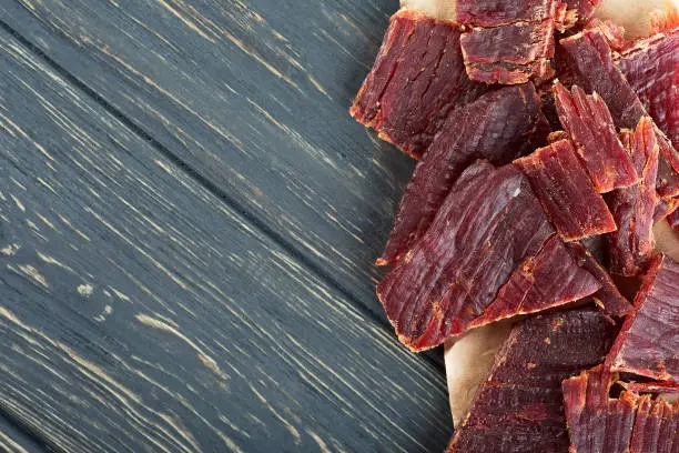 Spicy beef jerky on wooden background, top view.