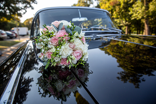 A wedding bouquet of roses and carnations on a black car hood.