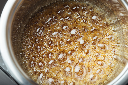 Boiling sugar syrup in a stainless steel pan. Boiling brown liquid in a metal container