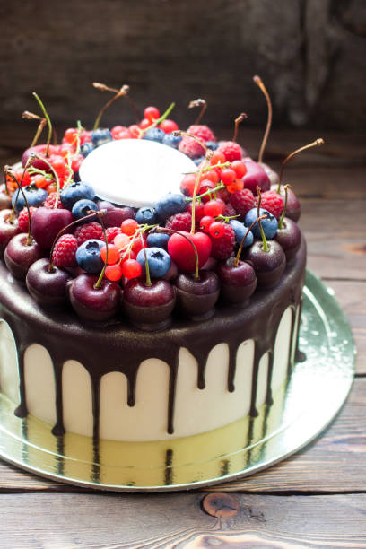 istock Birthday cake with melted chocolate, fresh cherry, raspberry, strawberry, red currant, blueberry on wooden background. 1248286192