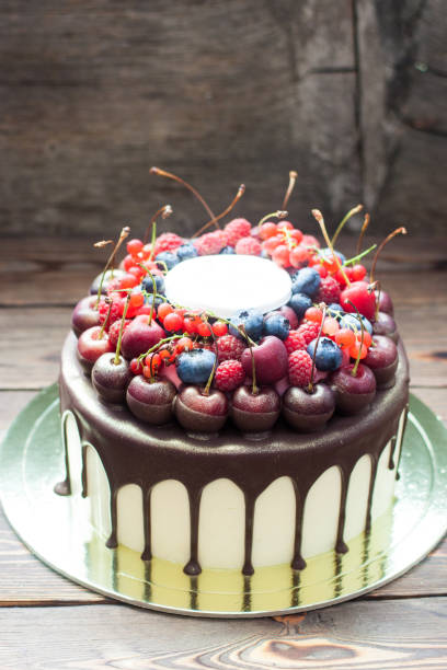 istock Birthday cake with melted chocolate, fresh cherry, raspberry, strawberry, red currant, blueberry on wooden background. 1248286512