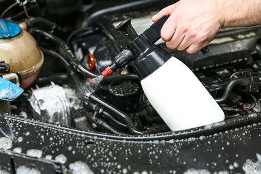 car engine washing close-up. car wash worker apply detergent on car engine. the mechanic's hand holds a spray bottle with detergent over the engine. Portable pressure water sprayer pump