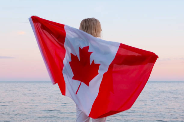 rückansicht frau winkt national canada flagge im freien ozean meer sonnenuntergang im sommer - kanada tag, land, patriotismus, unabhängigkeitstag 1. juli - canada day fotos stock-fotos und bilder