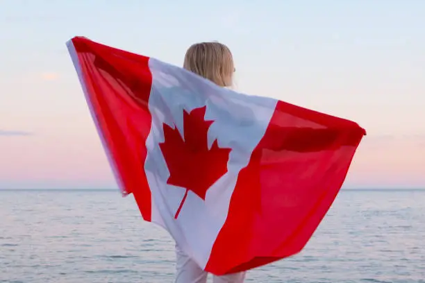 Photo of Back view woman waving national canada flag outdoors ocean sea sunset at summer - Canada day, country, patriotism, independence day 1th july