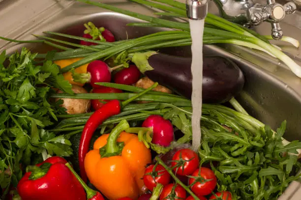 Photo of Vegetables in sink under running water.