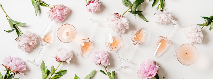 Rose wine variety layout. Flat-lay of rose wine in glasses and summer peony flowers over white background, top view. Summer drink for party, wine shop or wine tasting concept
