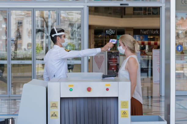shopping mall worker taking temperature of customers - infrared thermometer imagens e fotografias de stock