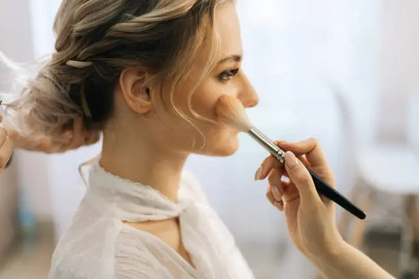 Photo of Close-up of make-up artist putting rouge on woman's cheek using brush