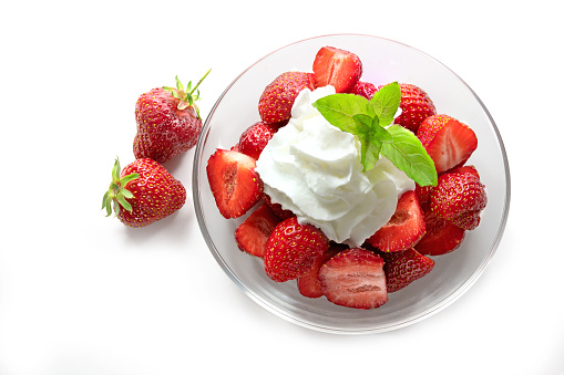 Dessert from fresh strawberries, whipped cream and peppermint garnish in a glass bowl, isolated with shadows on a white background, high angle view from above