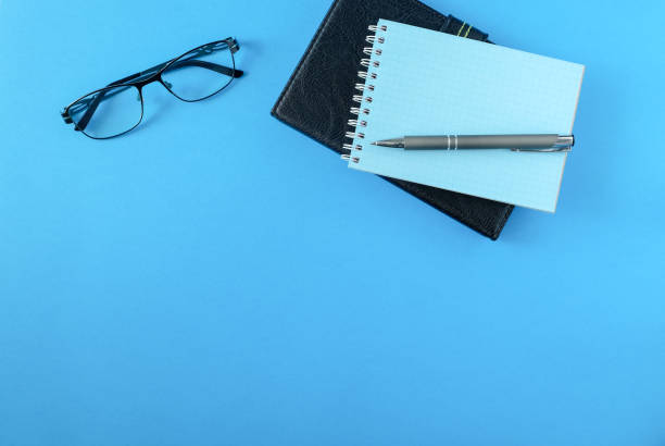 istock An e-book, a diary in a black leather cover, a notebook, glasses and a pen on a blue surface. 1248299609