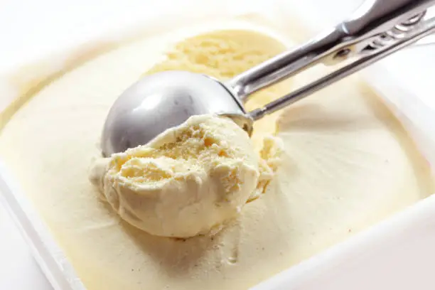 Photo of Metal scoop scrapes vanilla ice cream from the box, copy space