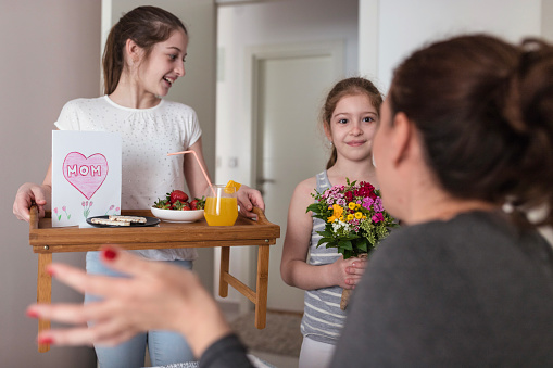 Kids bringing flowers and breakfast for her mother