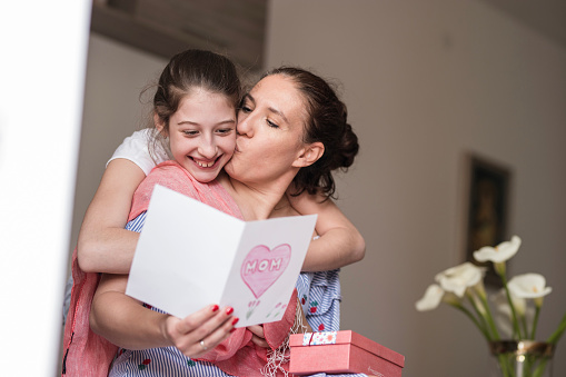 Smiling young girl hugging her mother after giving her a Mother's Day card