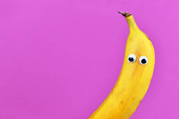 Half of funny ripe banana fruit with googly eyes on purple background with blank copy space
