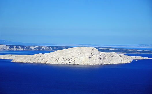 Aerial view of the big white rocky island surrounded by deep blue sea and the blue sky above lighted by sun. Scenic nature background