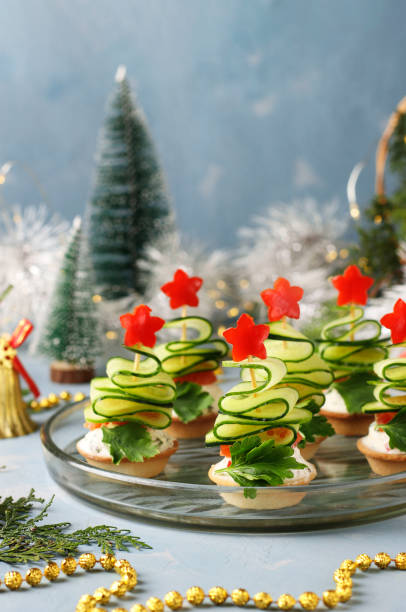 festliche kanapees in form von weihnachtsbäumen aus gurken und glockensternen auf hellblauem hintergrund mit zwei gläsern wein, closeup - canape appetizer gourmet salmon stock-fotos und bilder