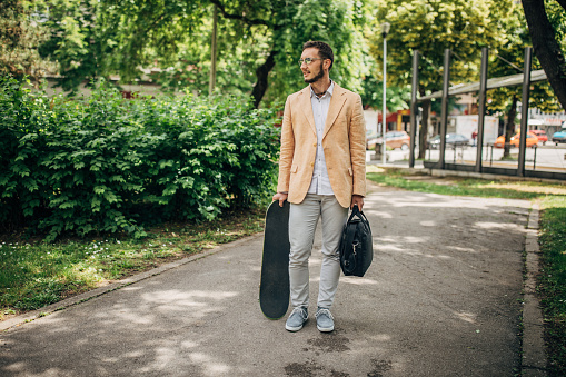 One men, young businessman with skateboard, standing in park.