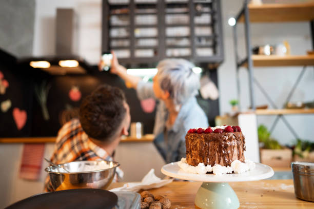 Couple taking selfies with a cake they made at their kitchen.