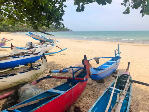 Colorfully painted outrigger fishing canoes on the beach of a tourist, honeymoon resort area of tropical Bali, Indonesia, Southeast Asia
